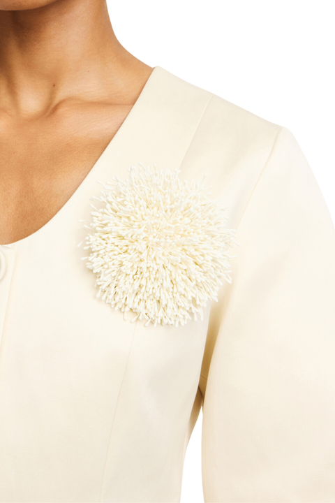 Close-up of a cream-colored top with a large, textured, anemone inspired brooch on the chest, worn by a model.