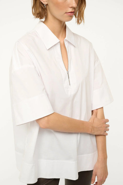 Detail shot of a woman wearing a white oversized short sleeve, collared tunic that features a zipper detail at the neck, paired with black capris.  