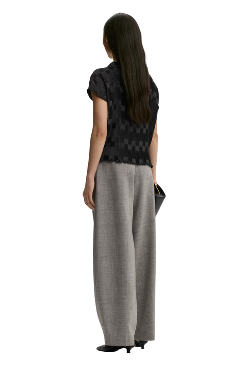 A woman shown from the back wearing a black patterned short-sleeve top and wide-leg gray trousers, standing against a plain white background.