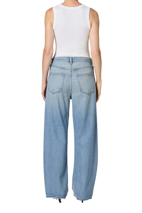 Person wearing light blue mid-rise jeans and a white tank top on a white background from the back