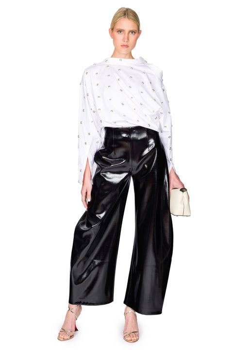 Model poses with handbag in white studded shirt and black patent pants.