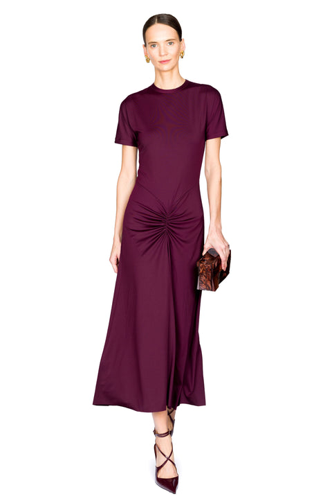 Woman posing wearing a burgundy midi dress with a scrunch detail holding a brown clutch on a white background