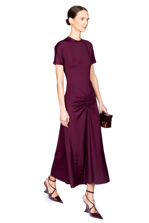 Woman walking wearing a burgundy dress holding a brown clutch with a white background