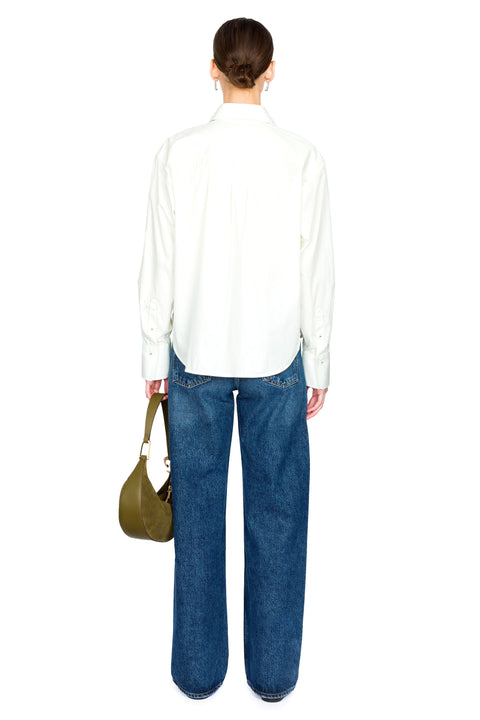 Woman showing the back of a light green poplin shirt and blue jeans holding a green bag on a white background