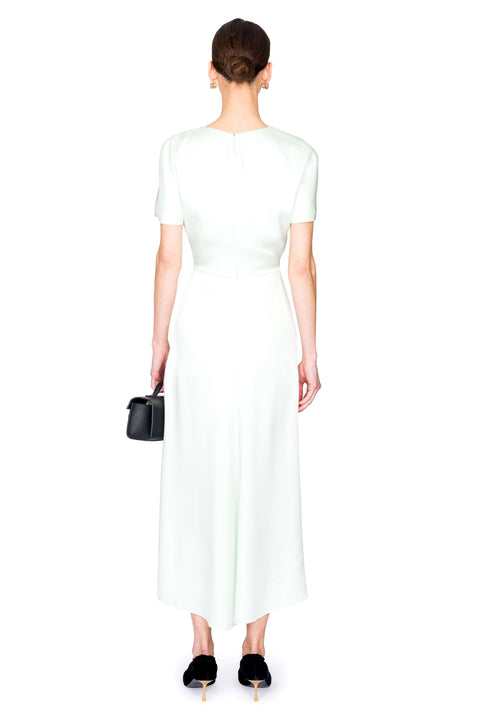 Woman facing away wearing  a light green dress holding a black handbag on a white background