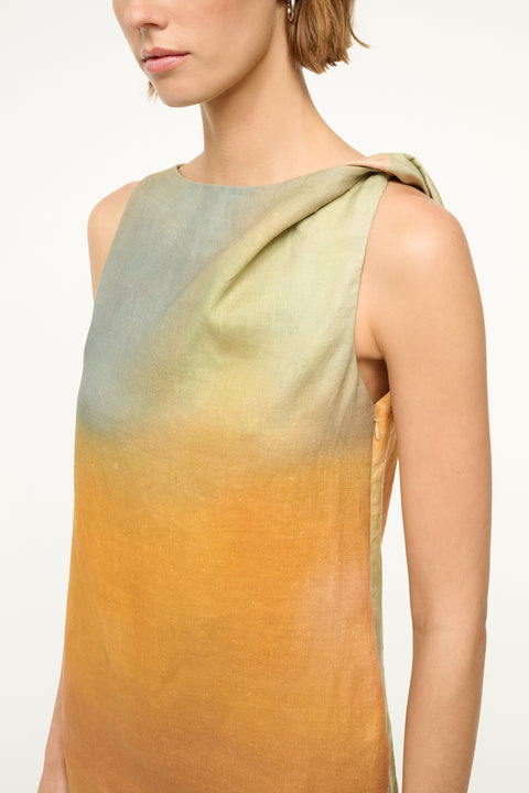 Close up of a woman wearing a sleeveless, pastel multicolor, mini shift dress that features a twist detail on one shoulder. 