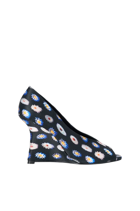 A black wedge shoe with an allover daisy floral print in white, blue, and yellow, shown from a side profile on a white background.