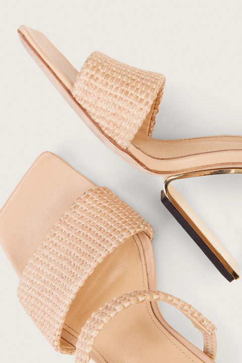 Detail shot of a pair of raffia heels that feature two slide in straps and a gold-toned suspended, hollow heel. 