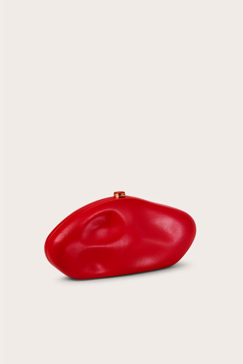 Side view of a red leather abstract sculptural clutch wit gold hardware. 