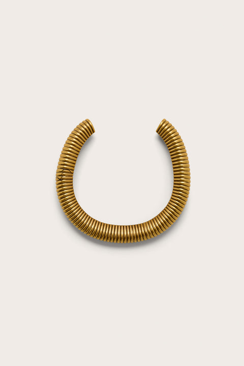 A gold toned, reeded choker that features an open back and hidden hinge, crafted with an antique brass finish. 