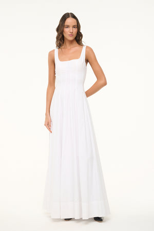 Woman wearing a sleeveless, white maxi dress that features a square neck, corset style paneling, and A-line skirt. 