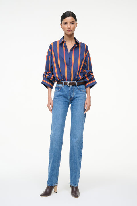 Woman wearing a blue and orange striped, long sleeve bodysuit with jeans and boots. 