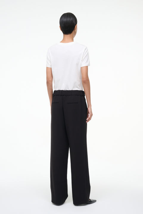 Back-facing person wearing a white top and black pants on a white background