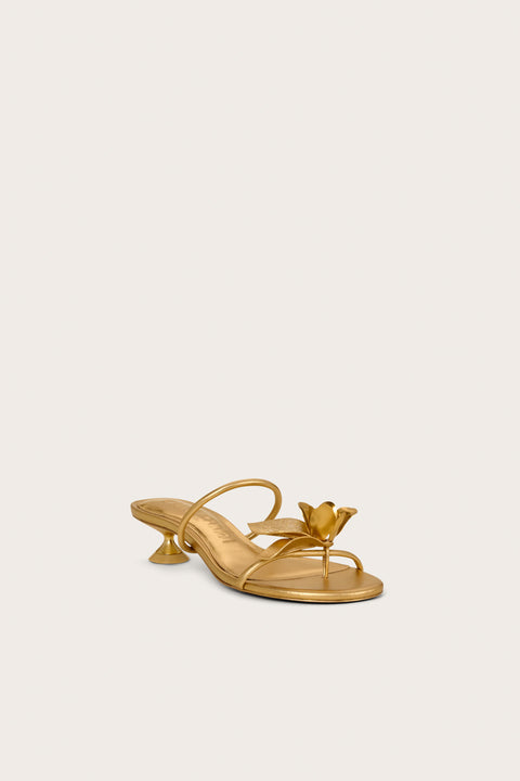 Front view of a a gold kitten heel that features an over-the-foot strap and a toe ring strap that has a gold flower applique.  
