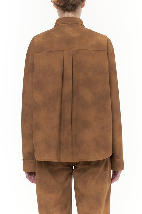 Back-facing woman wearing a brown leather workwear jacket with floral embellishments and silver snap closure. 