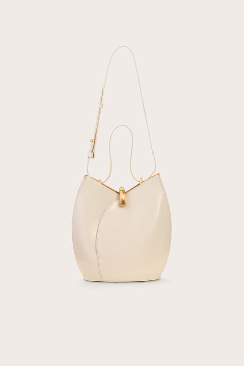 White leather shoulder bad that has a curved opening and resembles a tulip, featuring gold hardware and a shoulder and hand strap. 