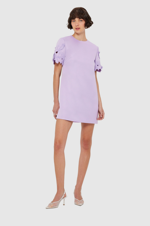 Woman posing a light purple mini dress with floral appliques on the sleeves on a white background
