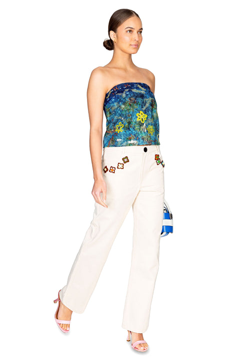 Model walking to the right showing the side of the flower crochet detailed jeans in cream.