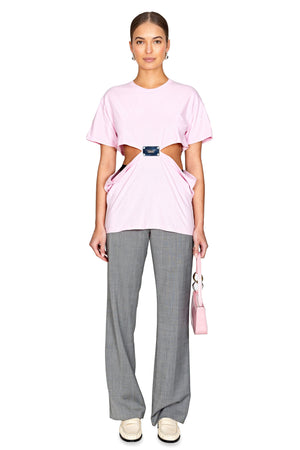 Model styled wearing the pink t shirt with silver metal logo plate in the center and open sides.