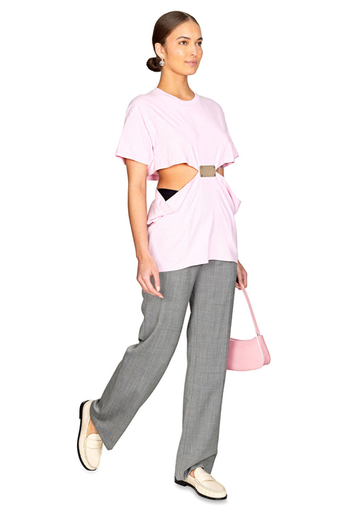 Model walking to the right showing the open sides of the pink t shirt with metal logo plate.