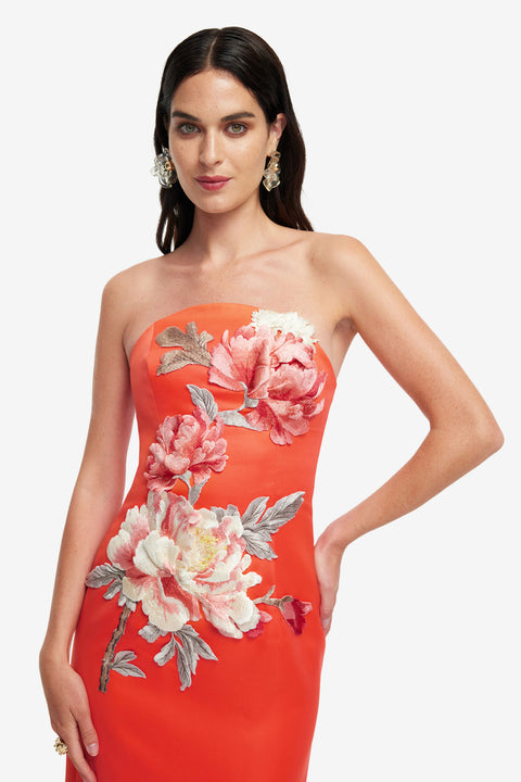 Up close of woman wearing a strapless orange dress with floral patterns on a white background.