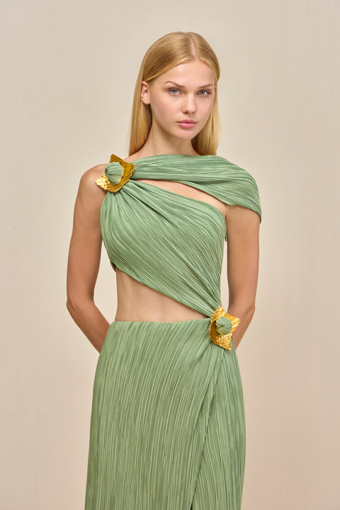 Close up of a woman wearing a green maxi dress crafted from plisse fabric that features a torso cutout and an asymmetric off-the-shoulder strap and gold-toned hardware details. 