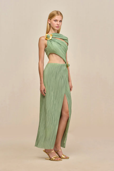 Side-facing woman wearing a green maxi dress crafted from plisse fabric that features a torso cutout and an asymmetric off-the-shoulder strap and gold-toned hardware details. 