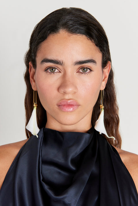 Woman wearing white calla lily inspired drop earrings on a gold threader chain. 