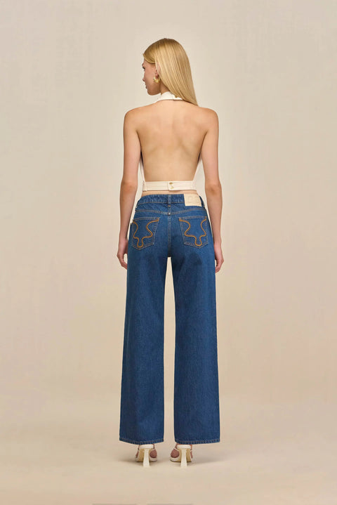 Back-facing woman wearing a cream, faux leather halter top with an open back, paired with blue jeans