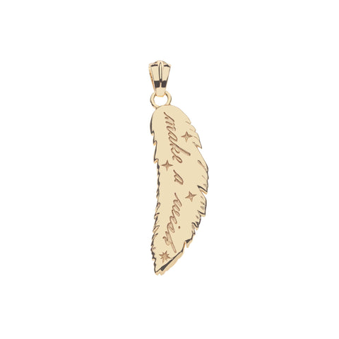 Back of a gold feather pendant with the inscription "Make a wish" and small star etchings. 