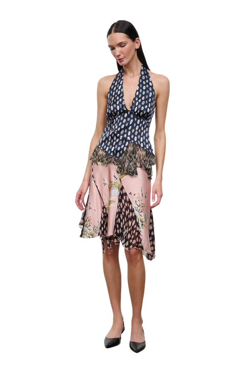 A woman modeling a sleeveless halter-neck top with a navy blue and white  pattern on the upper bodice and a pink, black, and beige floral print on the skirt, set against a plain white background.