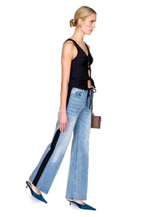 Woman wearing a black cutout top with a crystal pendant and black skirt with a brown bag on a white background from the side view.