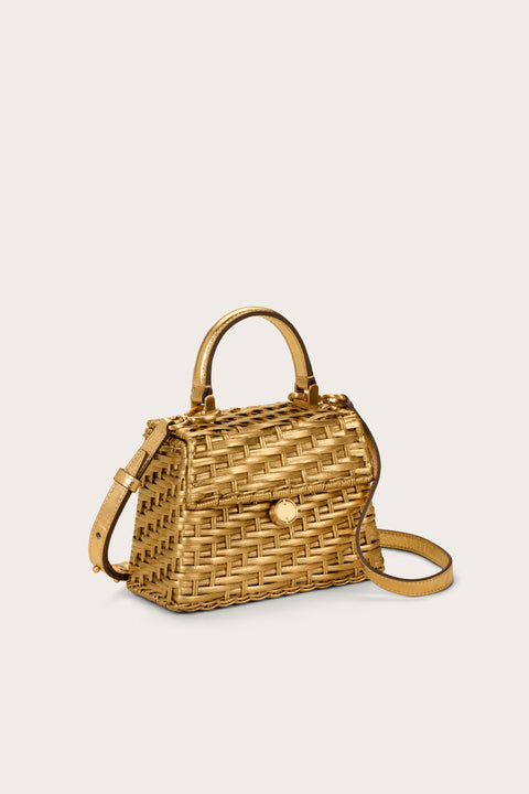 Side angle of a trapezoidal structured woven mini bag that features a gold-toned, metallic finish, with a top handle and gold-toned hardware, with a detachable crossbody strap.