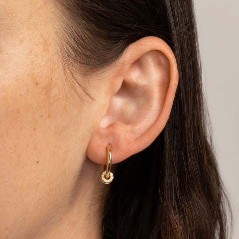 Woman wearing a small, yellow gold hoop earring with three yellow gold annulets, one pave with white diamonds. 