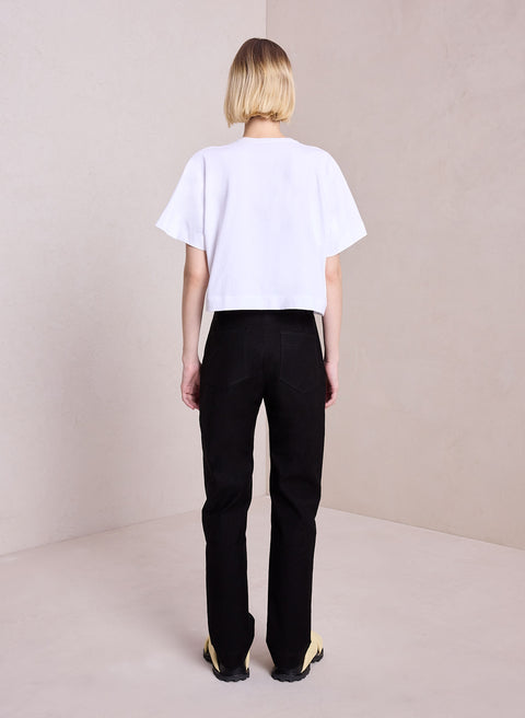 Model facing the back in the white Oliver Tee paired with black pants