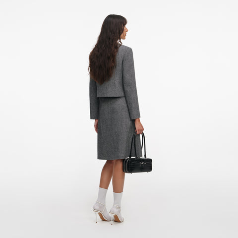Woman wearing a gray jacket and skirt holding a black handbag on a white background