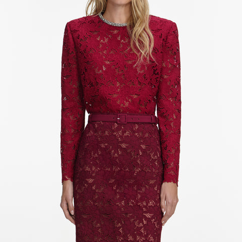 Up close look at long sleeve red lace top with crystal embellishment on the necklace and lace skirt with belt on a white background