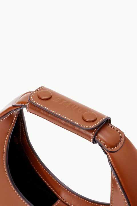 Detail shot of a brown leather mini handbag in the shape of a moon with a brown leather handle strap. 