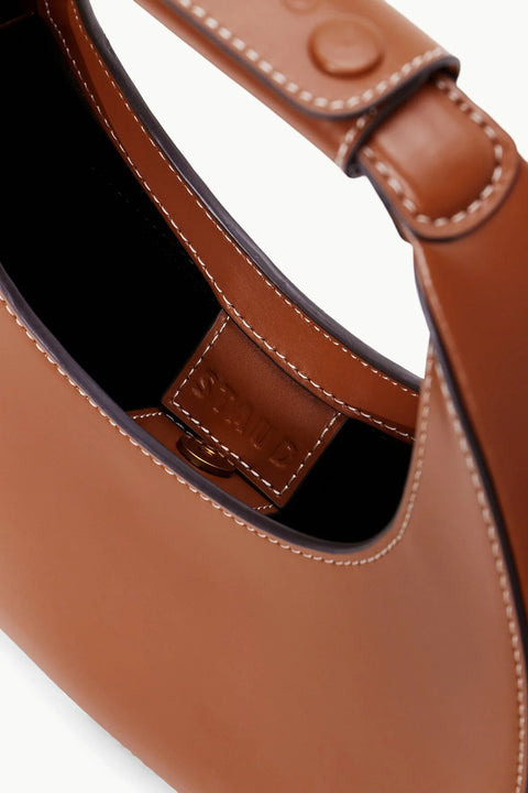 Inside shot of a small, brown leather, moon-shaped handbag with a magnetic closure. 