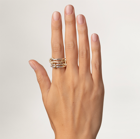 A woman's hand wearing a Spinelli Kilcollin ring that features a slim sterling silver band, a central 18k yellow gold band with channel set white diamonds, another slim sterling silver band, and a thicker sterling silver band, all connected by three 18k yellow gold connector rings. 