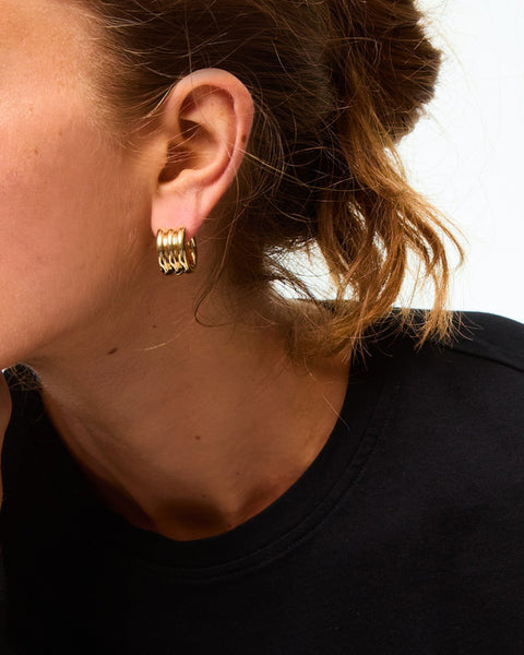Woman wearing a gold-toned huggie earring that features a triple tube design. 