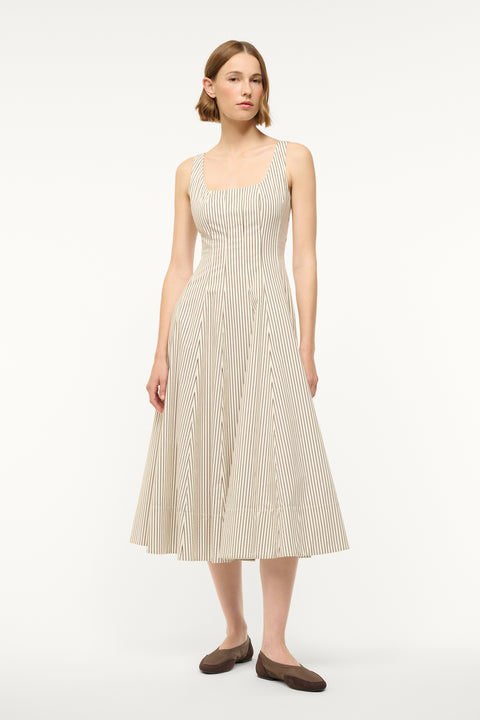 Woman wearing a midi dress that boasts a square neck, corset-style bodice, full, and full A-line skirt in a cream and brown micro stripe pattern, paired with flats. 