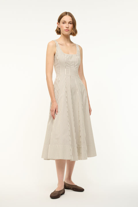 Side view of a woman wearing a midi dress that boasts a square neck, corset-style bodice, full, and full A-line skirt in a cream and brown micro stripe pattern, paired with flats. 
