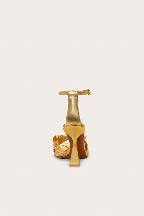 Back view of a gold sandal that features a comma heel and gold raffia straps. 