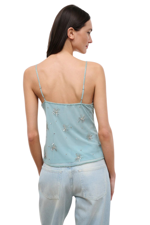 Woman wearing a light blue denim tank top with embellishments on a white background back angle