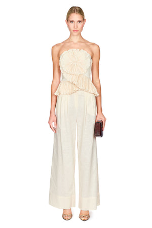 Woman wearing a strapless beige flower top with wide leg beige pants on a white background