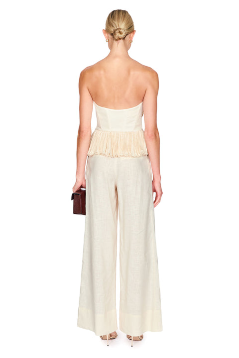 Woman wearing a strapless beige flower top with wide leg beige pants on a white background