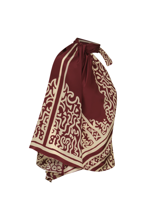 A burgundy and ecru patterned top with one draped sleeve and a halter tie-neck side angle