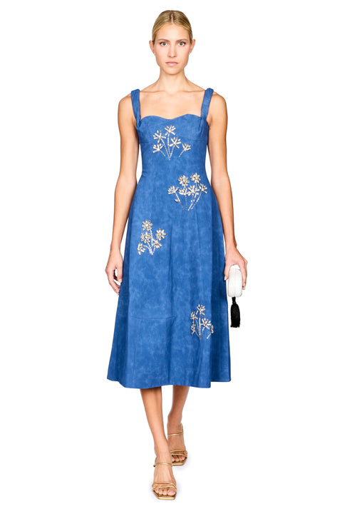 A woman modeling a blue midi dress with silver floral embroidery, standing against a plain white background.
