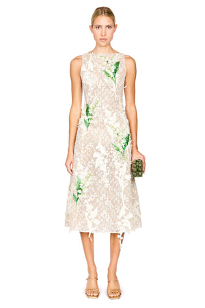 A model wearing a sleeveless cream lace midi dress with green floral applique, paired with gold high-heeled sandals, against a plain white background.